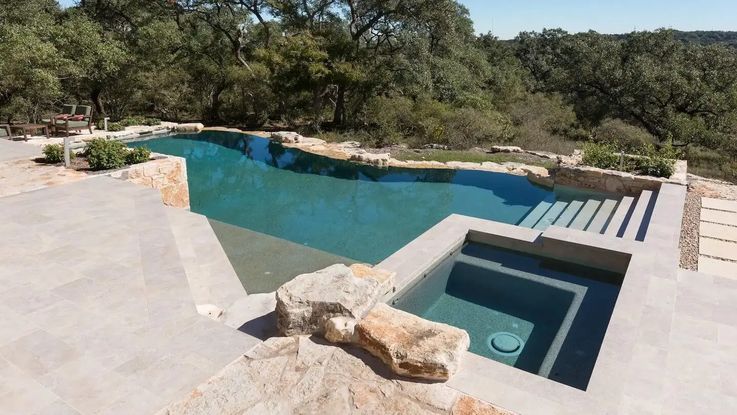 a modern pool with an organic look with a stone walkway overlooking a hill with trees